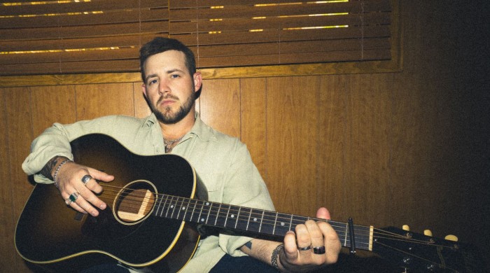 A man wearing a green shirt holding an acoustic guitar